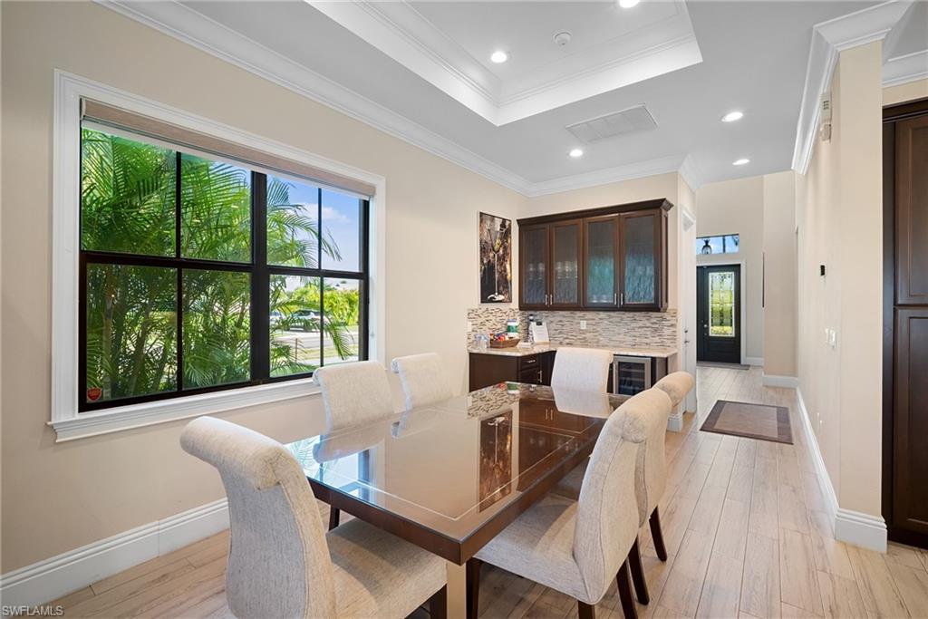 Dining room featuring light wood finished floors, a tray ceiling, crown molding, recessed lighting, and wine cooler