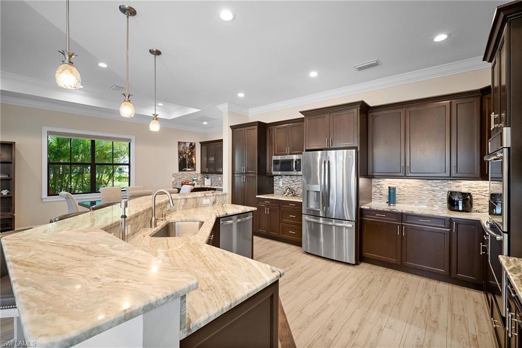 Kitchen with a kitchen island with sink, crown molding, pendant lighting, stainless steel appliances, and dark brown cabinetry