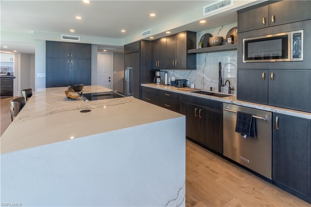 Kitchen with decorative backsplash, recessed lighting, light stone counters, stainless steel dishwasher, and a kitchen breakfast bar