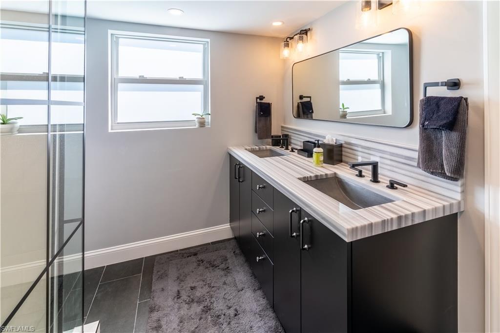 Full bathroom with double vanity, dark tile patterned floors, and a shower with shower door