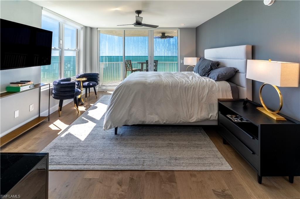 Bedroom with light wood-style flooring, access to exterior, expansive windows, a ceiling fan, and a water view