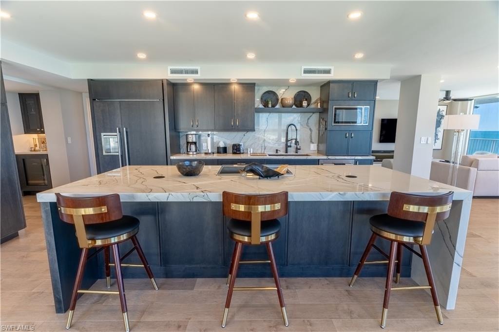Kitchen featuring tasteful backsplash, a large island with sink, recessed lighting, a breakfast bar area, and light stone counters
