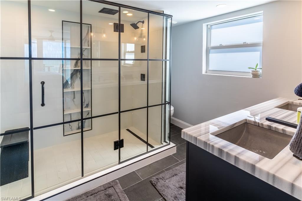 Full bath with double vanity, a shower stall, and dark tile patterned flooring