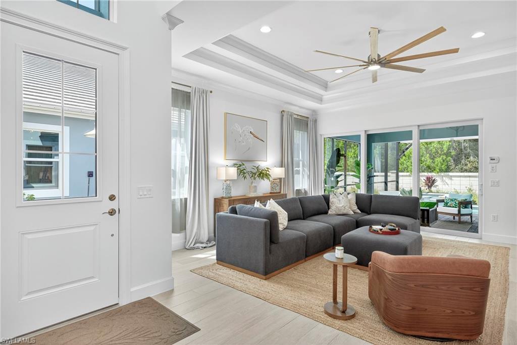 Living room featuring a raised ceiling, light wood-style flooring, ceiling fan, and recessed lighting