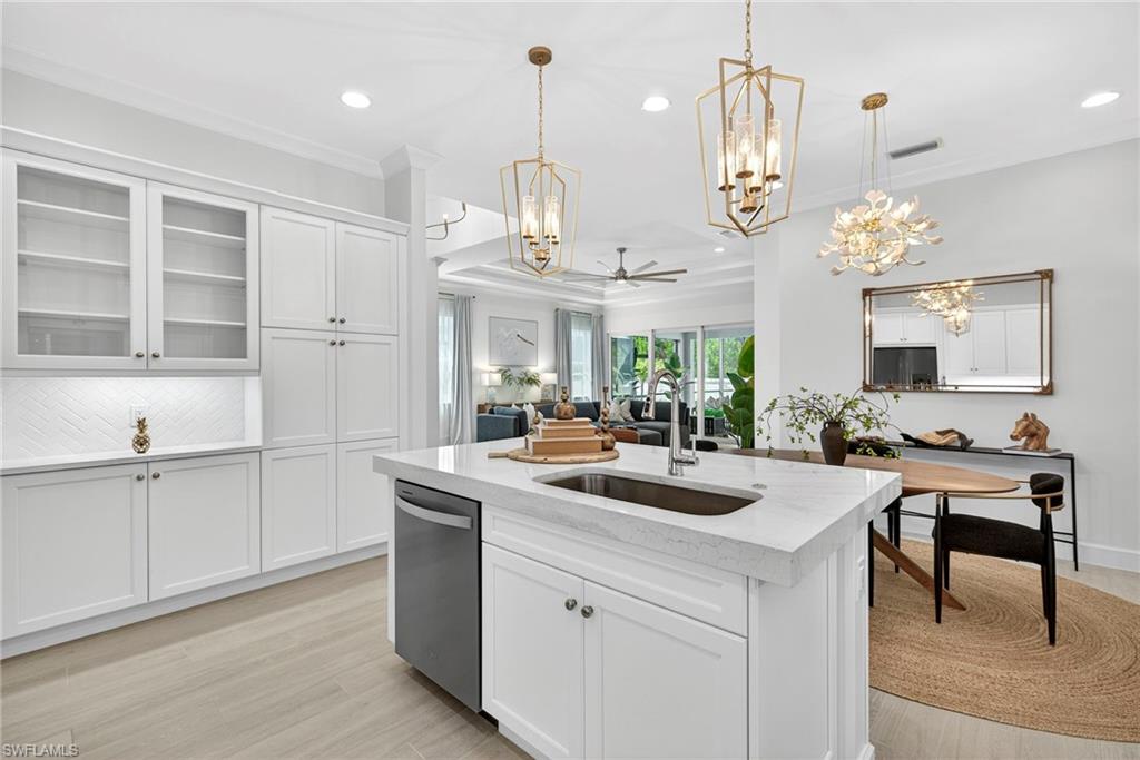 Kitchen featuring white cabinetry, ceiling fan, a kitchen island with sink, ornamental molding, and light stone countertops