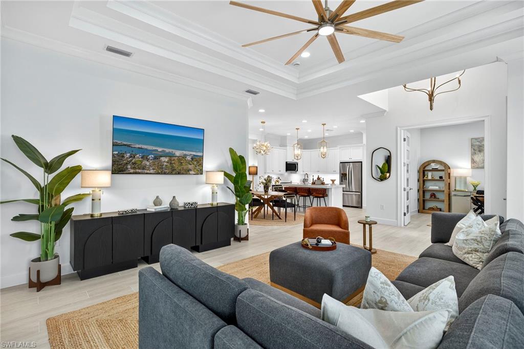Living area featuring a chandelier, light wood-type flooring, recessed lighting, a tray ceiling, and crown molding