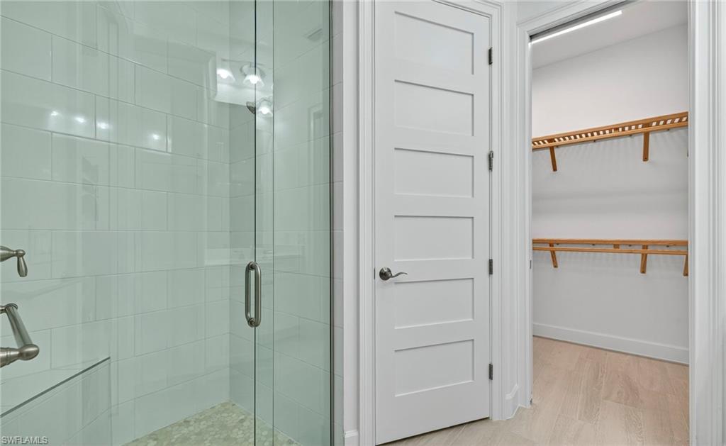 Full bath featuring a shower stall, light wood-style floors, and a spacious closet