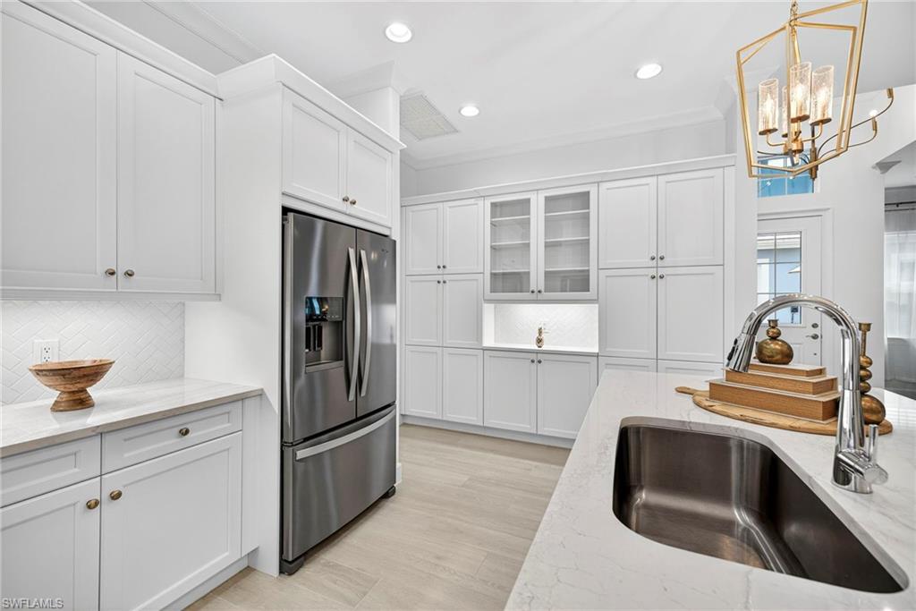 Kitchen featuring stainless steel refrigerator with ice dispenser, light stone countertops, glass insert cabinets, tasteful backsplash, and white cabinets
