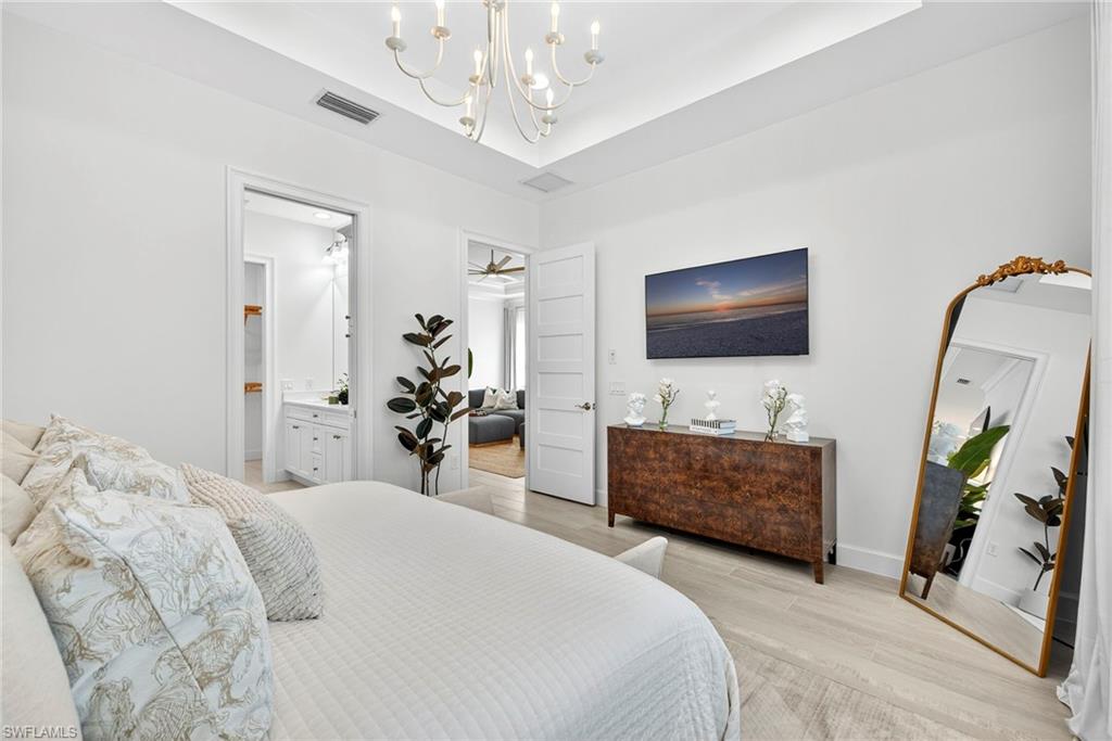 Bedroom featuring a chandelier, light wood-style flooring, a tray ceiling, and ensuite bath
