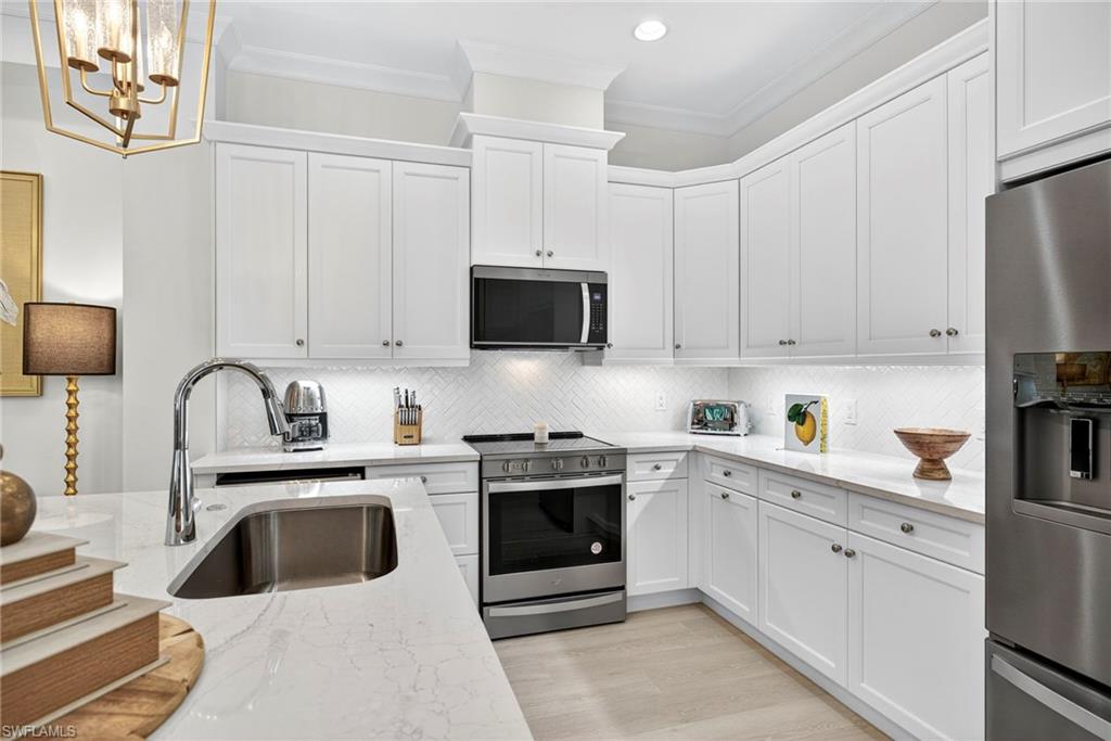 Kitchen with stainless steel appliances, decorative backsplash, white cabinetry, light stone counters, and crown molding