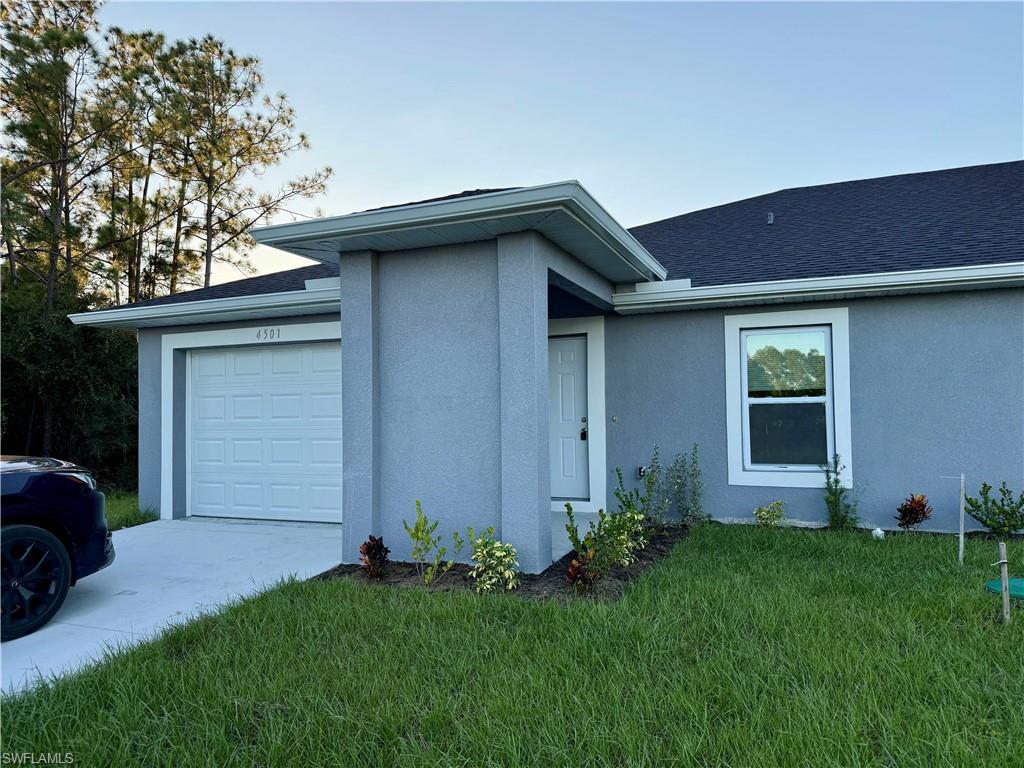View of front of property featuring a front yard, stucco siding, driveway, and a shingled roof