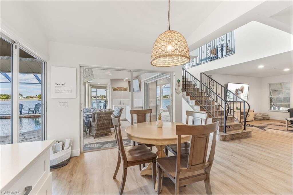 Dining room with light wood-type flooring, stairway, a water view, and a towering ceiling