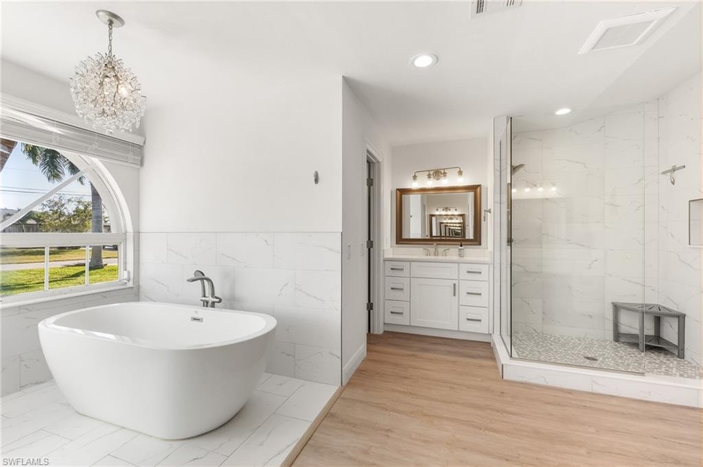 Bathroom with tile walls, vanity, a marble finish shower, a freestanding bath, and wainscoting
