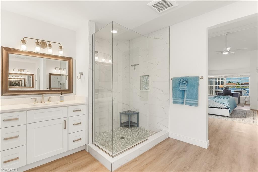 Ensuite bathroom featuring vanity, light wood-style flooring, a marble finish shower, and ceiling fan