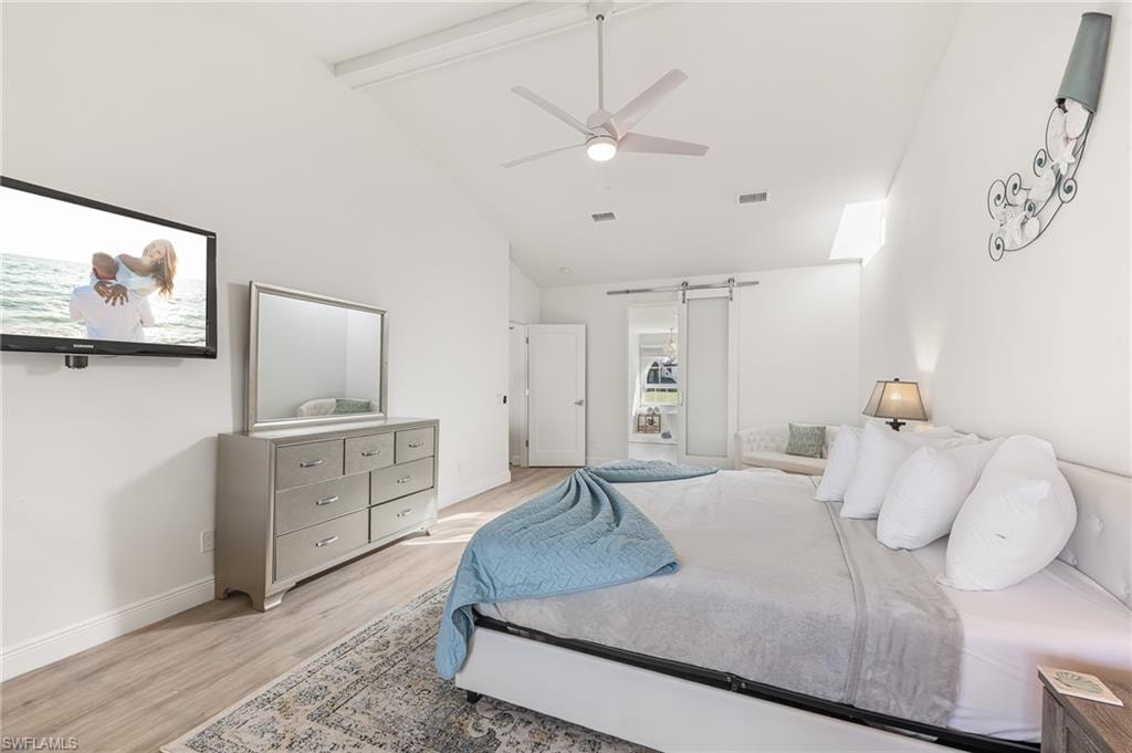 Bedroom featuring a barn door, beam ceiling, wood finished floors, high vaulted ceiling, and a ceiling fan