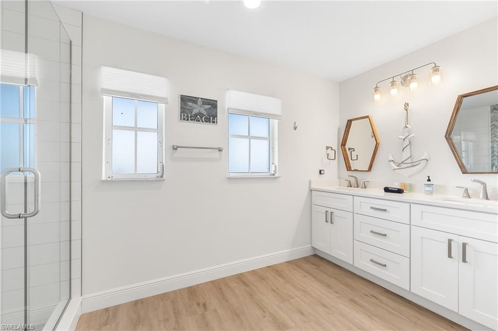Full bathroom with a stall shower, double vanity, and light wood-style floors