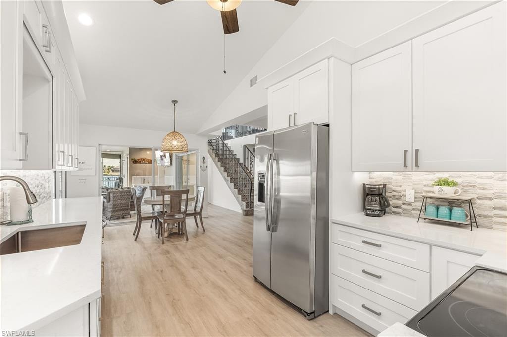 Kitchen with tasteful backsplash, stainless steel fridge with ice dispenser, white cabinets, and lofted ceiling
