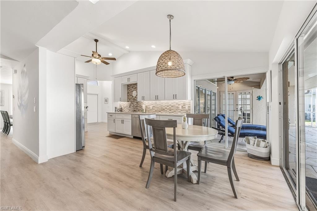 Dining space with lofted ceiling, light wood-type flooring, a ceiling fan, recessed lighting, and french doors