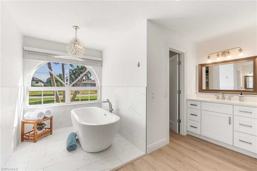 Bathroom featuring vanity, a freestanding bath, light wood finished floors, tile walls, and a chandelier