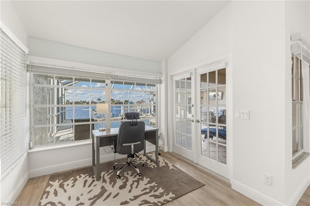 Home office with vaulted ceiling, light wood-type flooring, french doors, a water view, and a sunroom