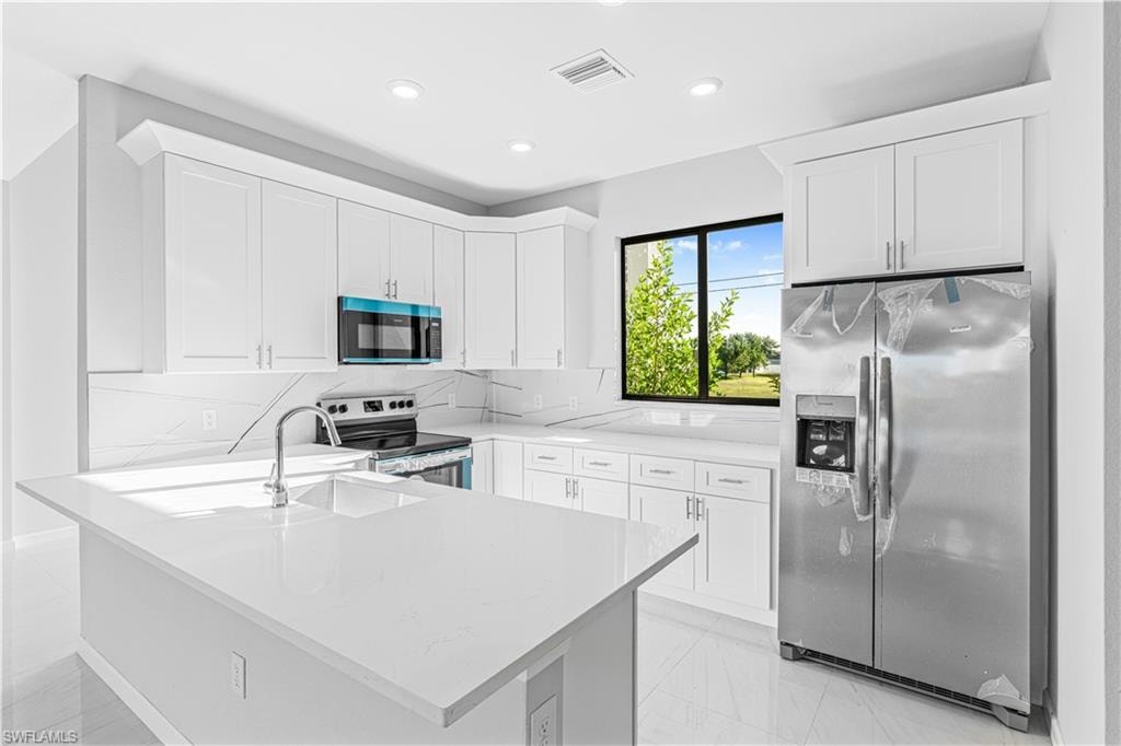 Kitchen featuring appliances with stainless steel finishes, white cabinetry, light stone countertops, light marble finish flooring, and recessed lighting