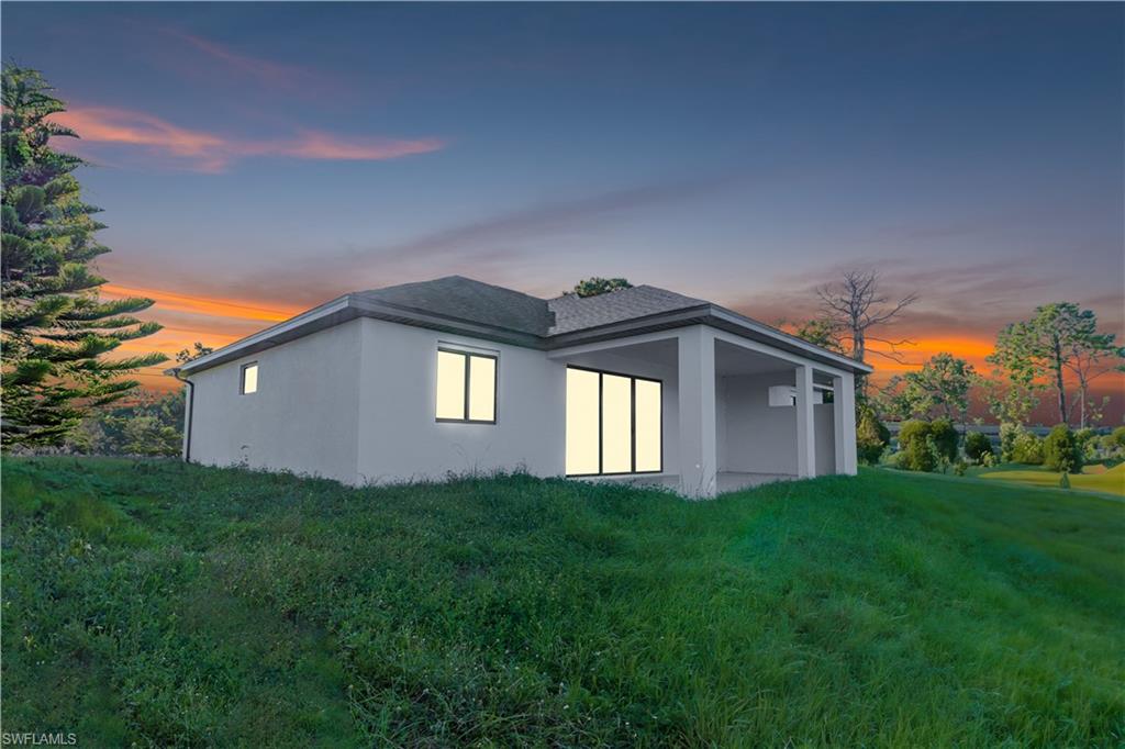 Back of house at dusk featuring stucco siding, a yard, and a patio area