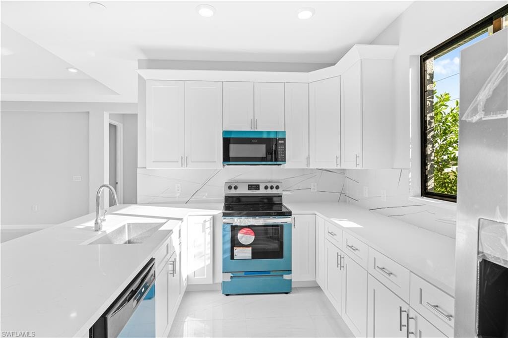 Kitchen with appliances with stainless steel finishes, a peninsula, tasteful backsplash, light stone countertops, and white cabinetry