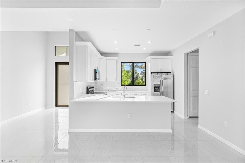 Kitchen featuring white cabinets, appliances with stainless steel finishes, light stone counters, a peninsula, and backsplash