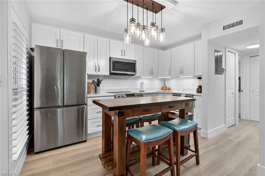 Kitchen featuring stainless steel appliances, light wood-style floors, decorative light fixtures, white cabinets, and butcher block counters