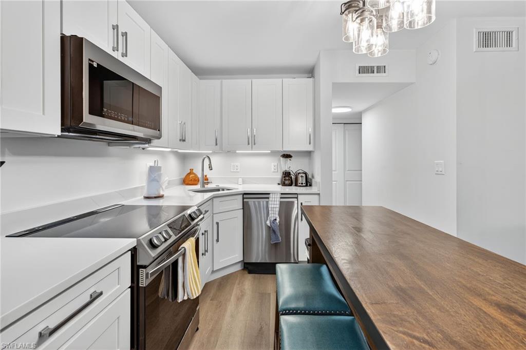 Kitchen featuring appliances with stainless steel finishes, dark wood-style floors, wood counters, white cabinetry, and decorative light fixtures