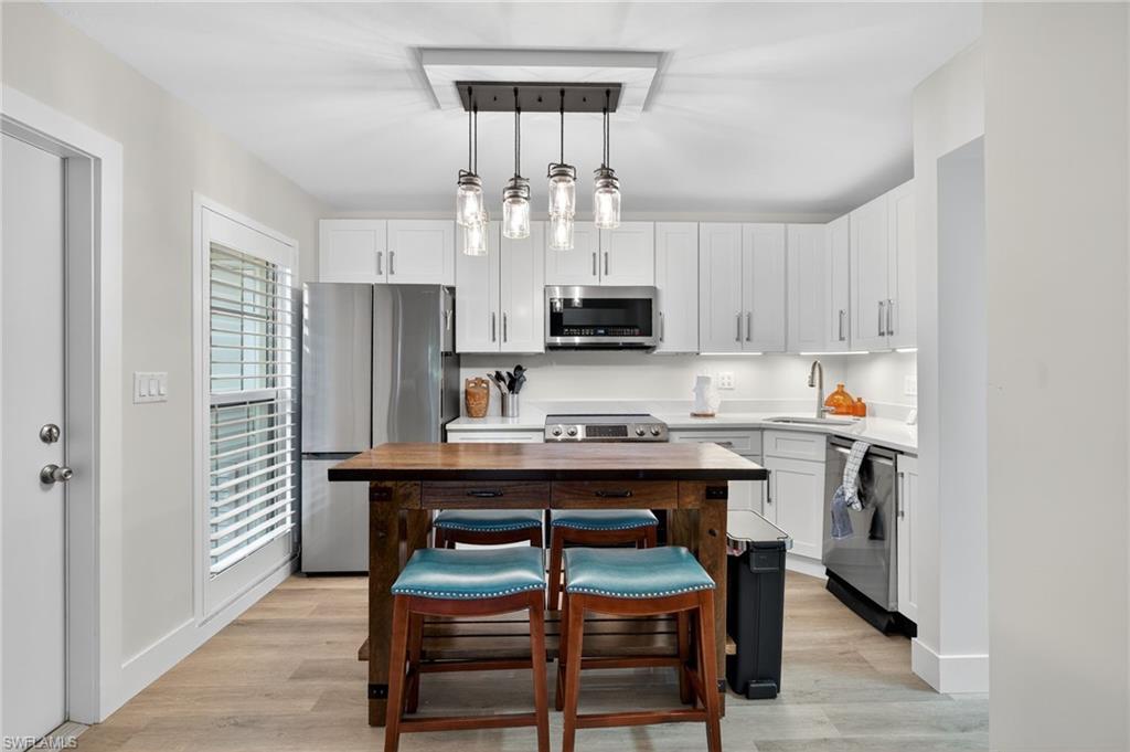Kitchen featuring appliances with stainless steel finishes, light wood-style floors, pendant lighting, and white cabinetry