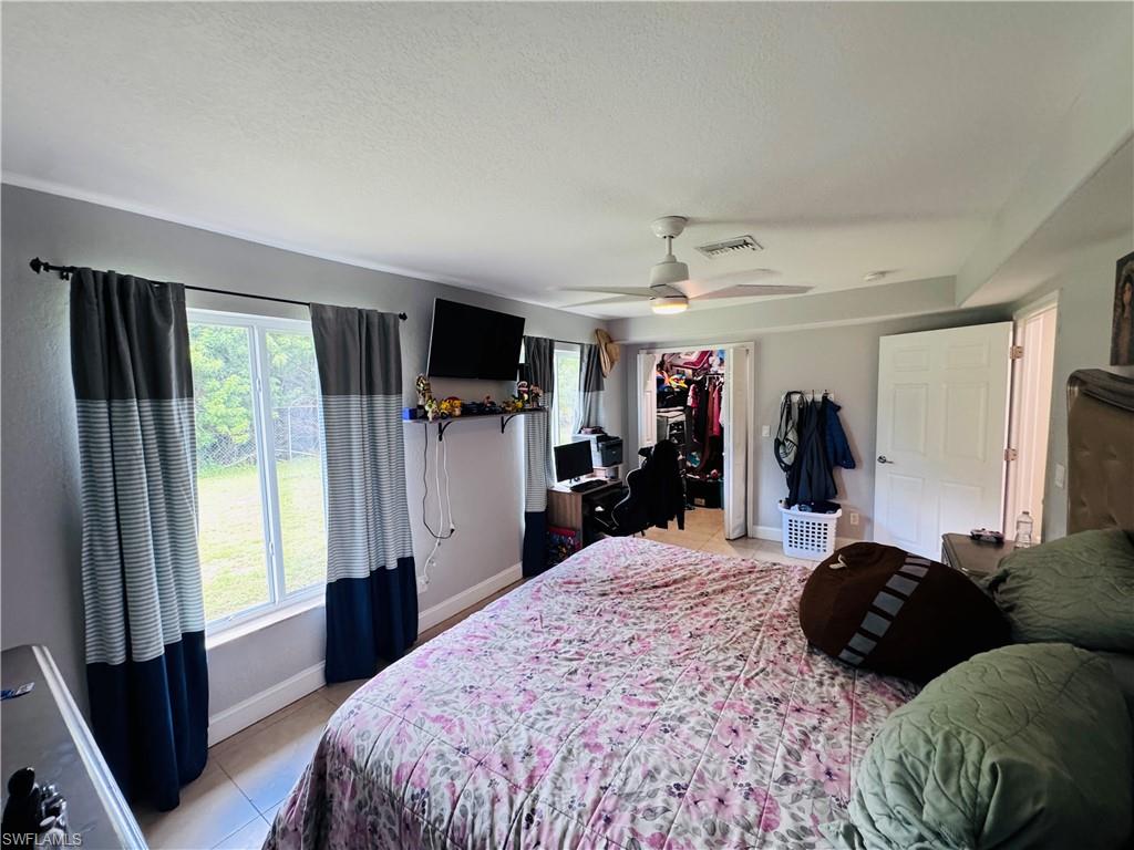 Bedroom with multiple windows, light tile patterned flooring, a walk in closet, a ceiling fan, and a textured ceiling