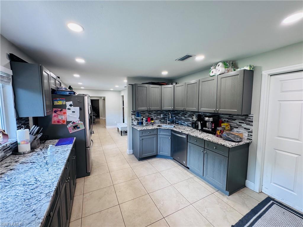Kitchen with light stone counters, tasteful backsplash, gray cabinetry, and recessed lighting