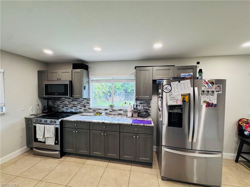 Kitchen featuring stainless steel appliances, tasteful backsplash, light tile patterned floors, light stone counters, and recessed lighting