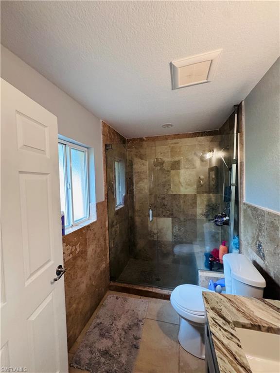 Bathroom featuring vanity, a shower stall, tile walls, a textured ceiling, and tile patterned flooring