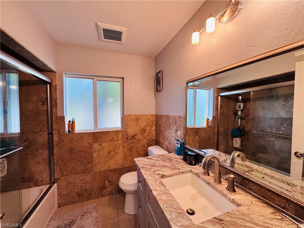 Full bath featuring tile walls, combined bath / shower with glass door, vanity, a textured ceiling, and a textured wall