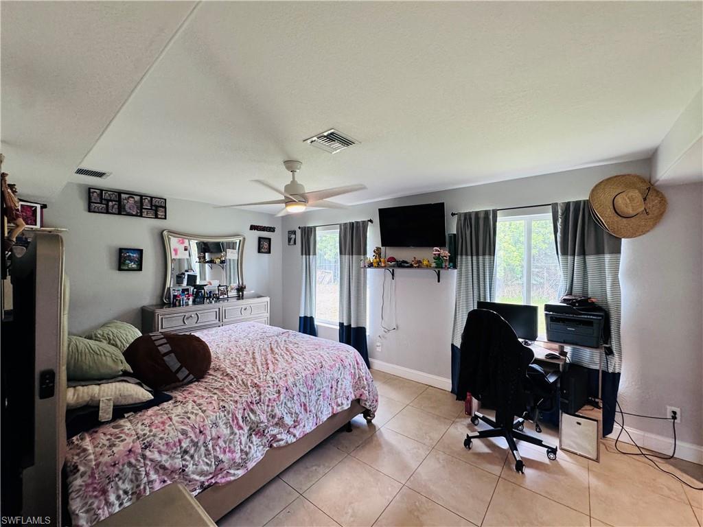 Bedroom with light tile patterned floors, an office area, and a ceiling fan