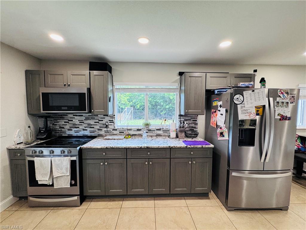 Kitchen featuring stainless steel appliances, decorative backsplash, light tile patterned flooring, recessed lighting, and light stone countertops