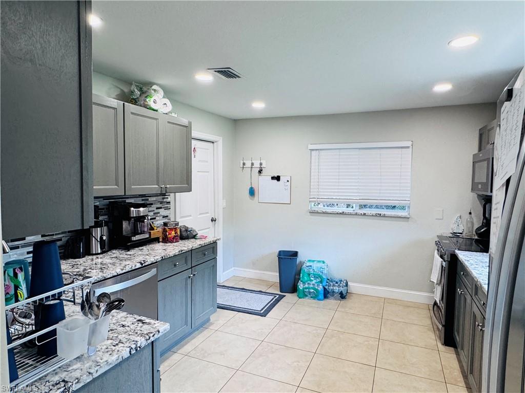 Kitchen with backsplash, stainless steel appliances, light stone counters, light tile patterned flooring, and gray cabinetry