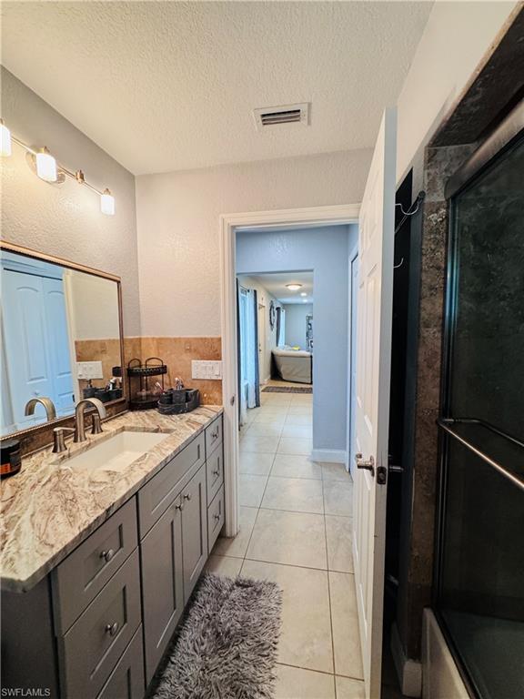 Bathroom featuring light tile patterned flooring, vanity, a textured ceiling, and a textured wall