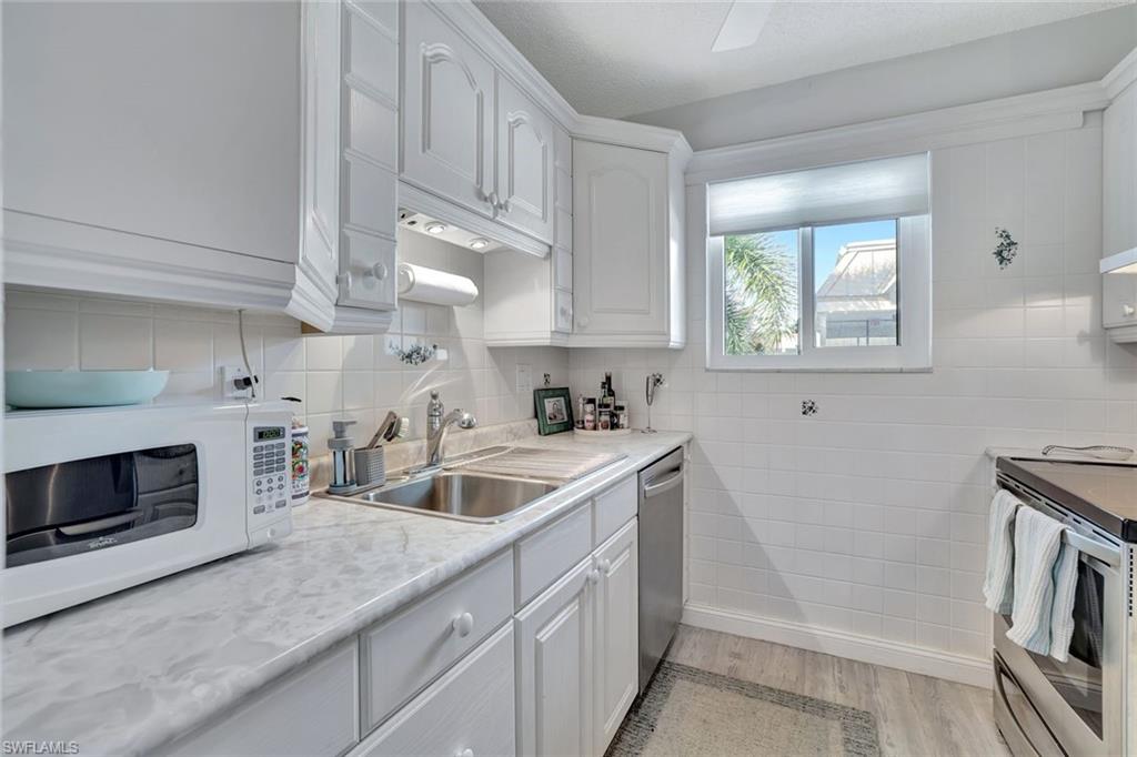 Kitchen with stainless steel appliances, white cabinetry, sink, and light wood-type flooring
