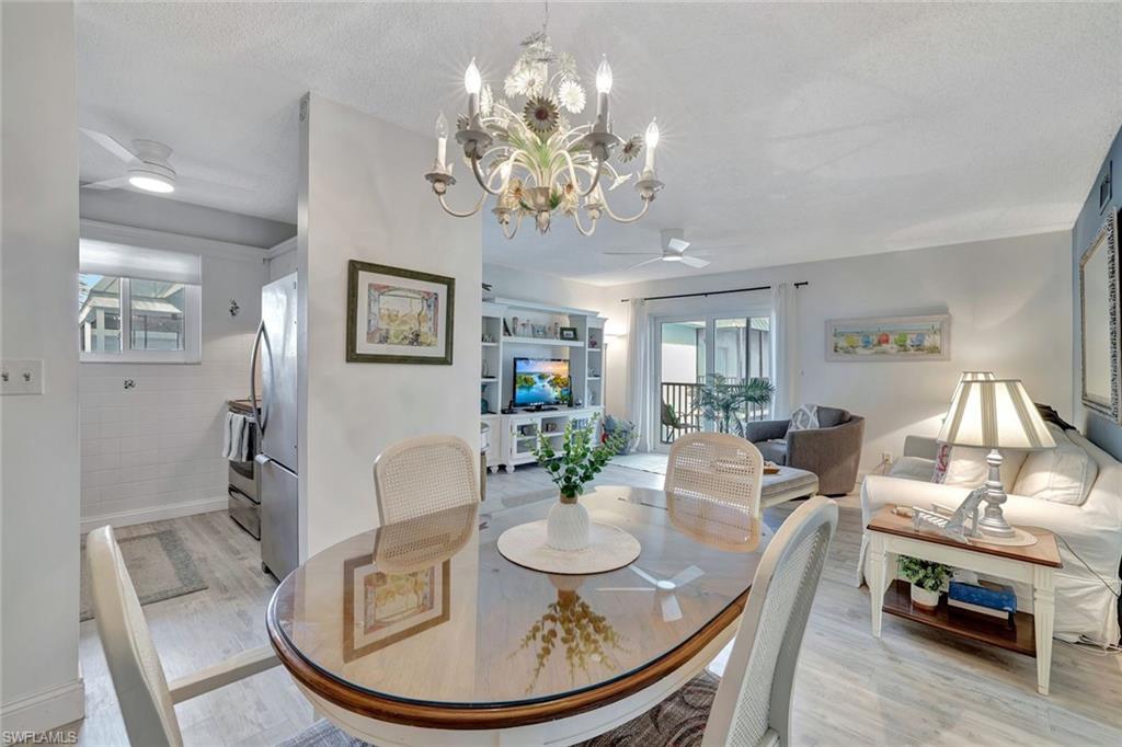 Dining area with light hardwood / wood-style flooring, a textured ceiling, ceiling fan with notable chandelier, and plenty of natural light