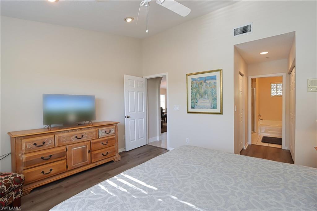 Bedroom with dark wood-type flooring, connected bathroom, and ceiling fan