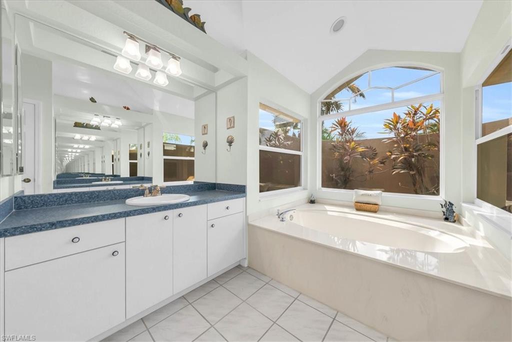 Bathroom featuring a bath, vanity, lofted ceiling, and light tile patterned floors