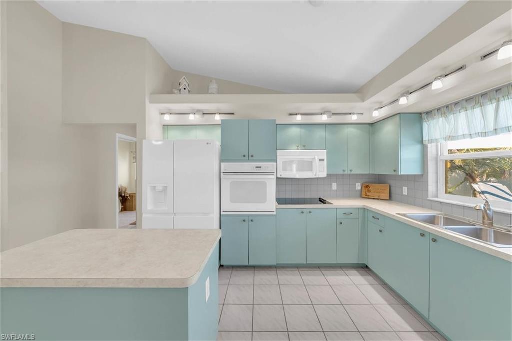 Kitchen with light tile patterned floors, white appliances, light countertops, decorative backsplash, and a kitchen island