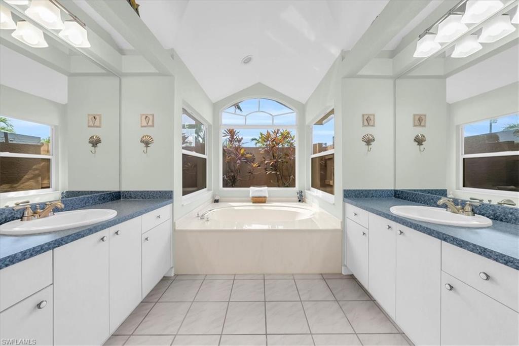 Bathroom with a garden tub, light tile patterned flooring, plenty of natural light, two vanities, and vaulted ceiling