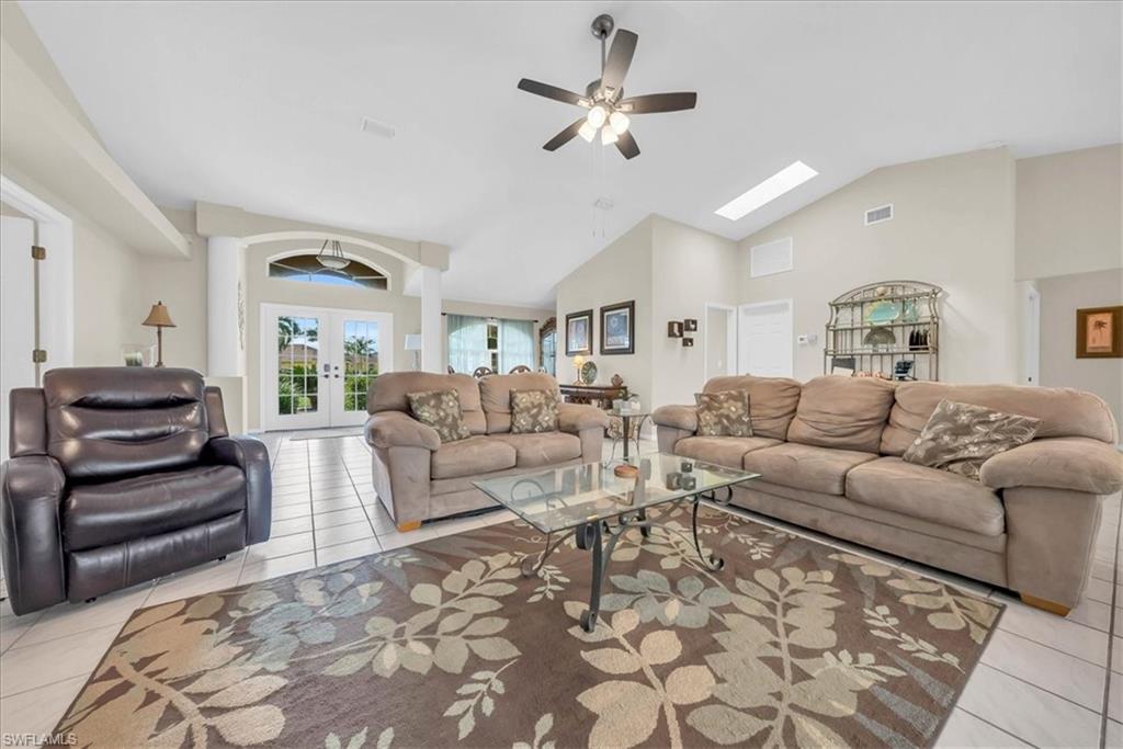 Living room with light tile patterned floors, french doors, a skylight, a ceiling fan, and high vaulted ceiling