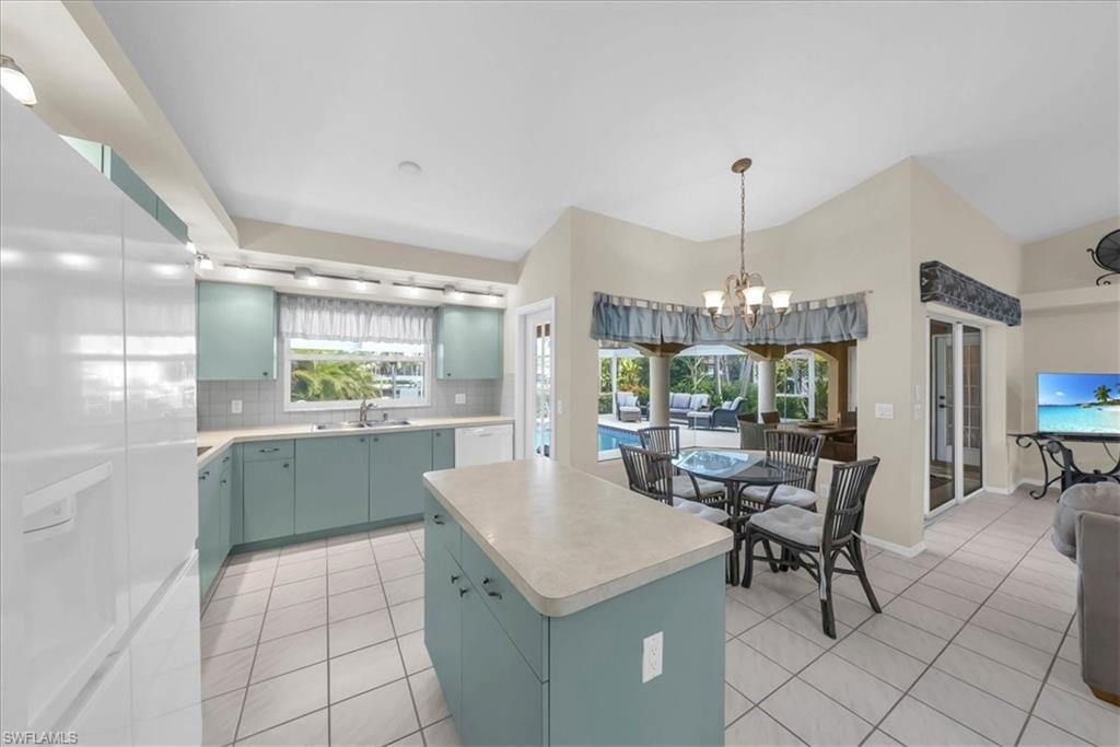 Kitchen featuring white appliances, decorative backsplash, light countertops, a center island, and light tile patterned floors