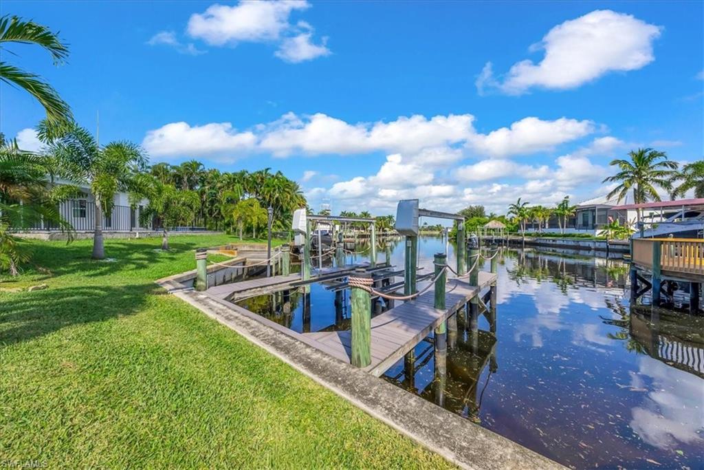 Dock featuring boat lift, a yard, and a water view