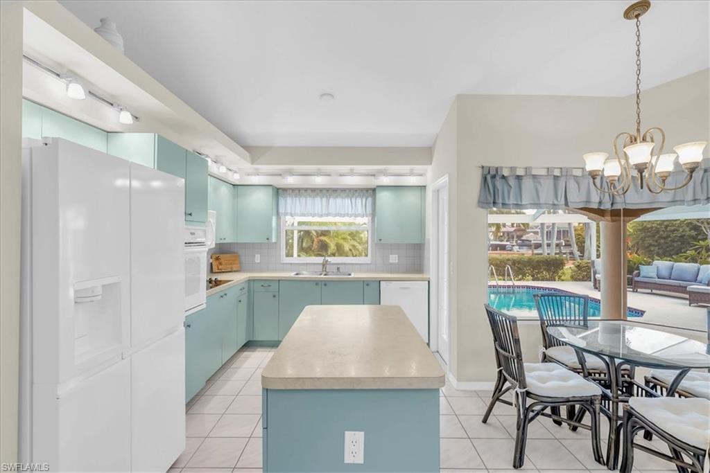Kitchen with white appliances, blue cabinetry, light countertops, hanging light fixtures, and a kitchen island